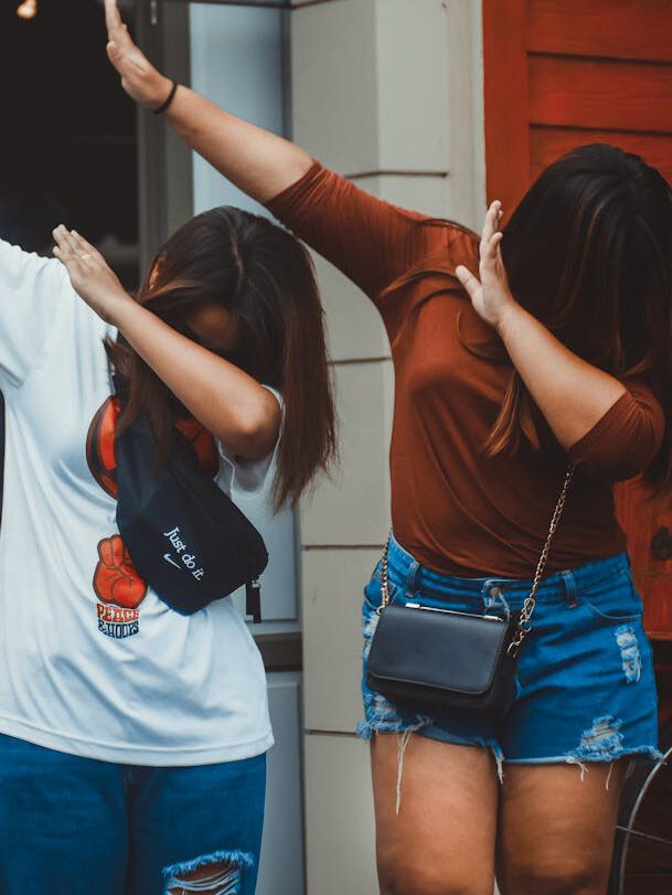 Two women in casual attire dabbing outdoors, expressing fun and friendship.