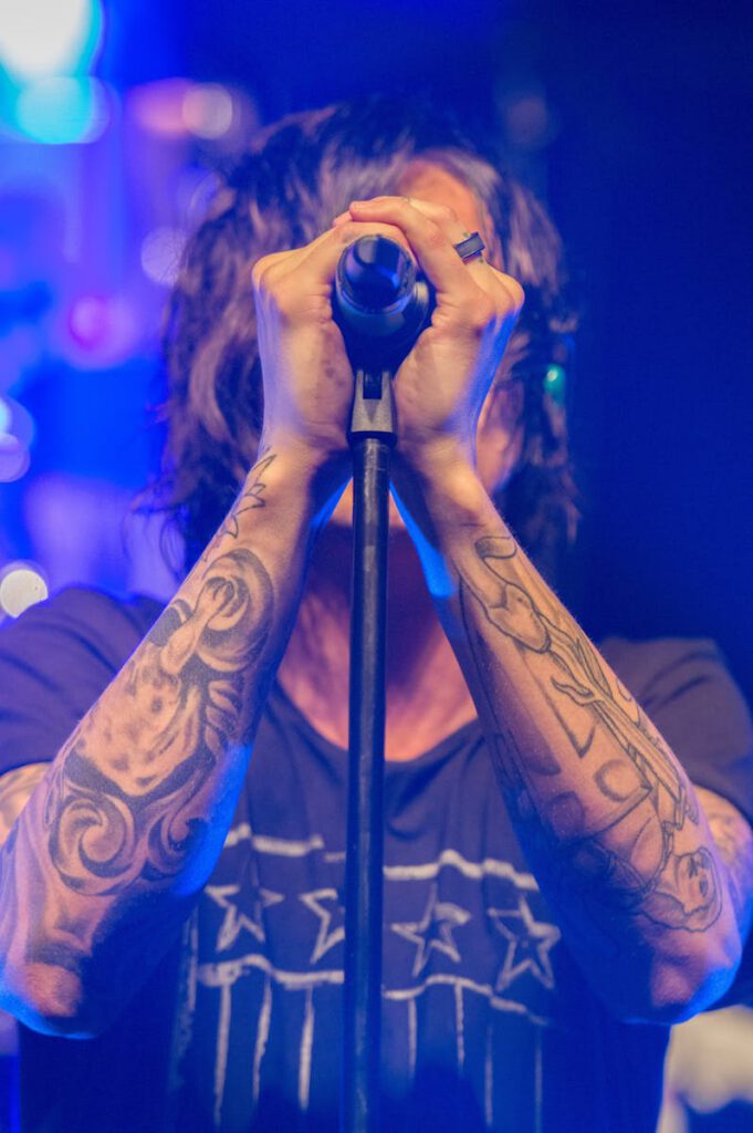 Young tattooed male musician passionately performs on stage illuminated by vibrant lights.